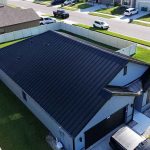 House with metal roofing installed, surrounded by green grass